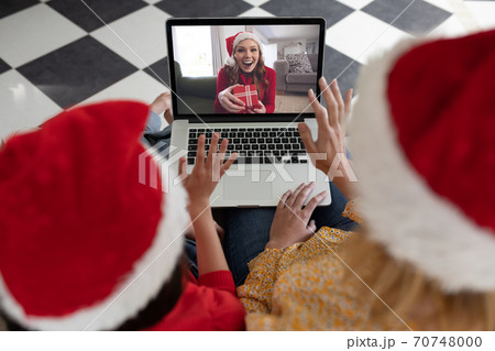 Woman and daughter in Santa hats having a video chat with another woman on laptop at home Woman and daughter in Santa hats having a video chat with another woman on laptop at home 70748000