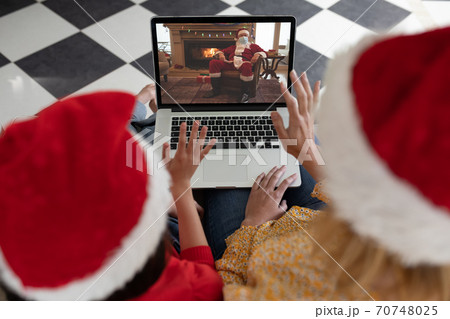 Woman and daughter in Santa hats having a video chat with another woman on laptop at home 70748025