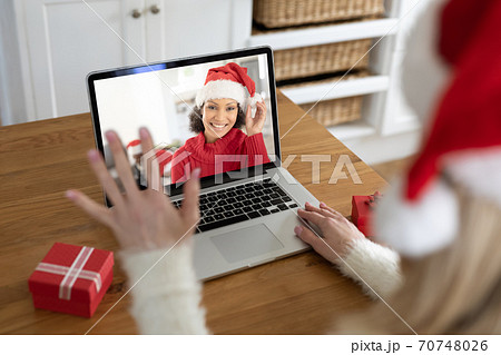 Woman in Santa hat waving while having a video chat with another woman on her laptop at home 70748026