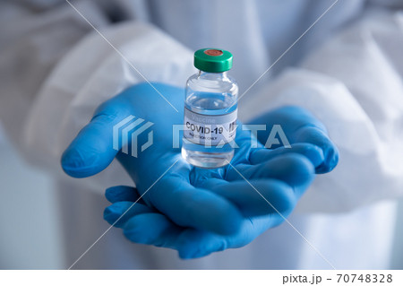 Close up of Health worker wearing protective gloves holding a vial bottle with Covid-19 text Close up of Health worker wearing protective gloves holding a vial bottle with Covid-19 text 70748328