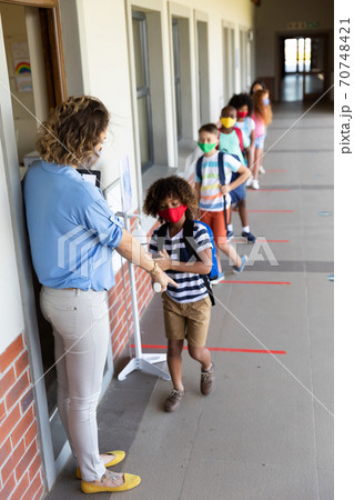 Female teacher wearing face mask pointing boy to stand on the marker 70748421