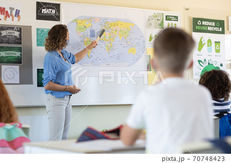 Female teacher wearing face mask teaching geography to students in class 70748423