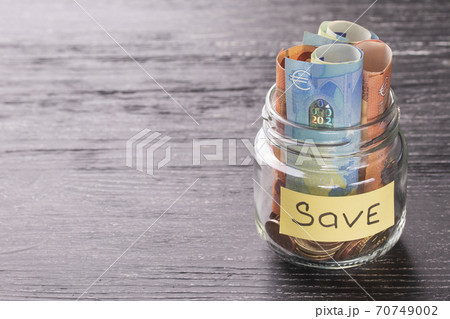 Euro notes and coins in a glass jar on a black wooden table with shiny reflection on a glossy surface. Money saving concept Euro notes and coins in a glass jar on a black wooden table with shiny reflection on a glossy surface. Money saving concept 70749002