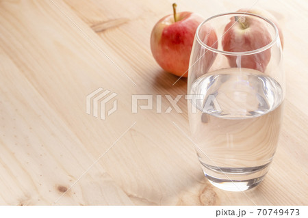 An image of a glass half full of water, standing on a wooden table, the apples are in the background. The concept of healthy eating and losing weight An image of a glass half full of water, standing on a wooden table, the apples are in the background. The concept of healthy eating and losing weight 70749473