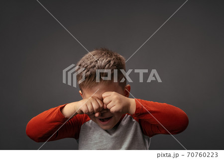 Crying little boy expresses sad emotions. Upset child rubs eyes with fists isolated on gray background. Problem concept Crying little boy expresses sad emotions. Upset child rubs eyes with fists isolated on gray background. Problem concept 70760223