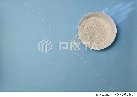Wheat flour in a white deep plate, a little awake on a blue background. Wheat flour in a white deep plate, a little awake on a blue background. 70760569