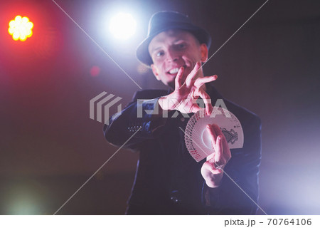 Magician showing trick with playing cards. Magic or dexterity, circus, gambling. Prestidigitator in dark room with fog 70764106