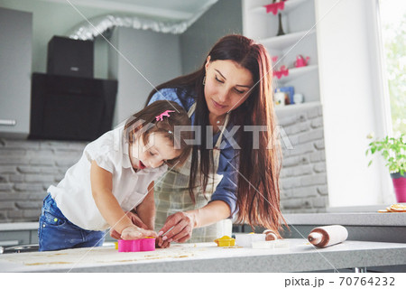 Happy family in the kitchen. Holiday food concept. Mother and daughter preparing the dough, bake cookies. Happy family in making cookies at home. Homemade food and little helper 70764232