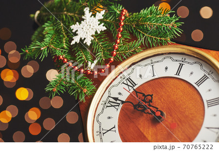 Happy New Year at midnight 2018, Old wooden clock with holiday lights and fir branches Happy New Year at midnight 2018, Old wooden clock with holiday lights and fir branches 70765222
