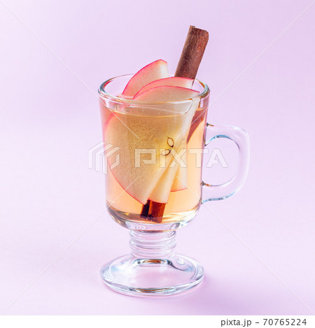 Glass of white glogg or mulled wine with apple slices and cinnamon stick on pink background, square 70765224
