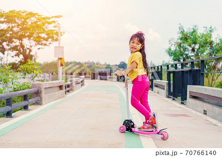 Little child girl to ride scooter in outdoor sports ground on sunny summer day. Little child girl to ride scooter in outdoor sports ground on sunny summer day. 70766140