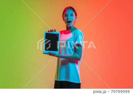 Young caucasian girl's portrait on gradient green-orange studio background in neon light 70769099