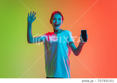 Young caucasian girl's portrait on gradient green-orange studio background in neon light Young caucasian girl's portrait on gradient green-orange studio background in neon light 70769101