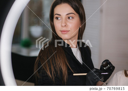 Portrait of professional female brow master in black robe with black gloves use brush and henna for eyebrows Portrait of professional female brow master in black robe with black gloves use brush and henna for eyebrows 70769815