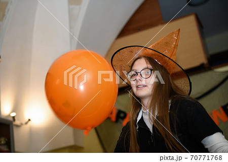 Girl in halloween hat is having fun and playing with orange and black Halloween baloons Girl in halloween hat is having fun and playing with orange and black Halloween baloons 70771768