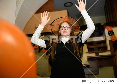 Girl in halloween hat is having fun and playing with orange and black Halloween baloons Girl in halloween hat is having fun and playing with orange and black Halloween baloons 70771769