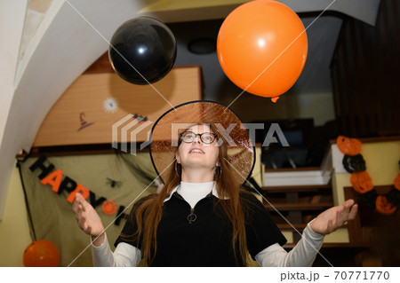 Girl in halloween hat is having fun and playing with orange and black Halloween baloons Girl in halloween hat is having fun and playing with orange and black Halloween baloons 70771770