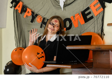 A girl in a Halloween make-up congratulates her friends and family on Halloween with a video call via a laptop A girl in a Halloween make-up congratulates her friends and family on Halloween with a video call via a laptop 70772110