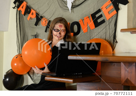 A girl in a Halloween make-up congratulates her friends and family on Halloween with a video call via a laptop A girl in a Halloween make-up congratulates her friends and family on Halloween with a video call via a laptop 70772111