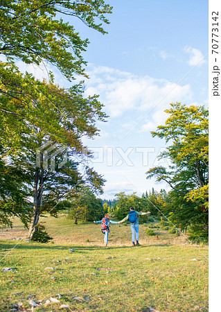 Beautiful couple walking with backpacks on the green meadow, while traveling high in the mountains during the summer time. Rear view 70773142