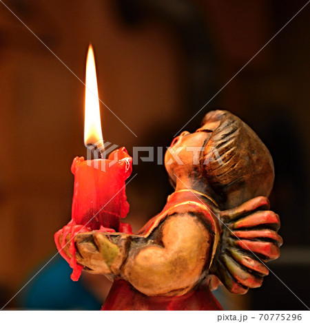 Wooden angel with a burning candle in his arms. 70775296