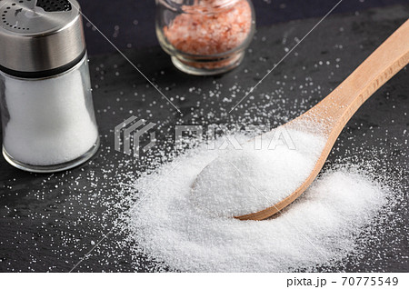 White sea salt for cooking food in Small glass bottles and wooden spoons on a stone tray background. 70775549