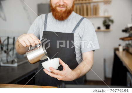 Coffee Business Concept - handsome bearded man in apron making coffee while standing at cafe Coffee Business Concept - handsome bearded man in apron making coffee while standing at cafe 70776191