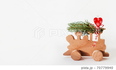 Wooden train with tied fir tree branches and red heart decoration. Cute symbol of Christmas tree brought home for New Year celebration. Winter holiday spirit. Copy space on white background. 70779940