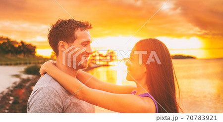 Happy couple in love embracing at sunset glow on Florida beach summer vacation background. Asian woman with arms around neck of caucasian boyfriend. Horizontal crop 70783921