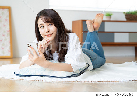 リビングで寝転がりながらスマホを見る笑顔の若い女性 70791069