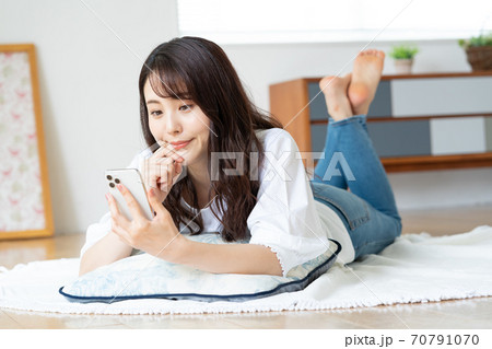 リビングで寝転がりながらスマホを見る笑顔の若い女性 70791070