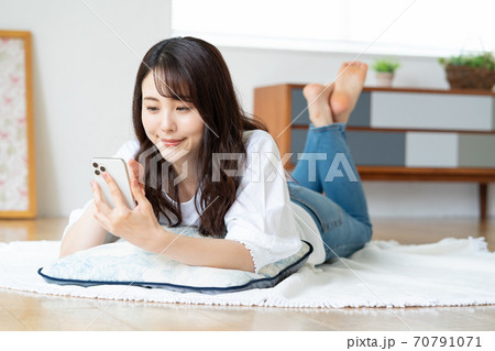 リビングで寝転がりながらスマホを見る笑顔の若い女性 70791071
