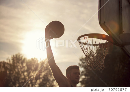 Young man jumping and making a fantastic slam dunk playing streetball, basketball. Urban authentic. 70792877