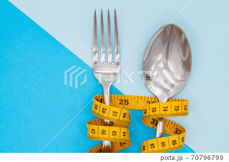 Fork and spoon is strung by a ribbon for measuring on a colored background. Symbol of diet and weight loss Fork and spoon is strung by a ribbon for measuring on a colored background. Symbol of diet and weight loss 70796799