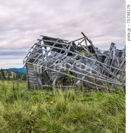 Close up stack of wooden planks of old shed up in mountains with cloudy sky and dried grass around. 70798176