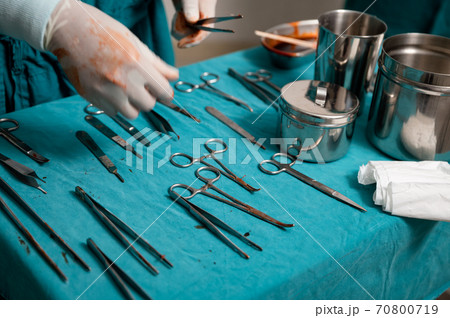 Surgeon hand wear medical gloves choosing surgical instruments on a table in operating room Surgeon hand wear medical gloves choosing surgical instruments on a table in operating room 70800719