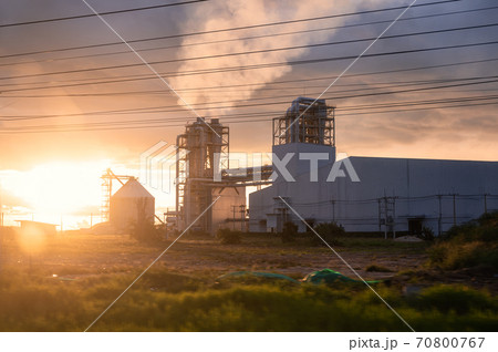 Sunset over Industrial pipe building of fiberboard factory working with release smoke from chimney 70800767