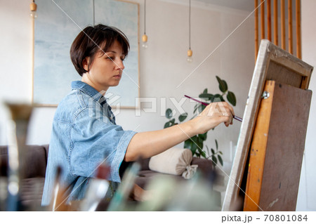 Concentrated short-haired female artist painting on cotton canvas with oil paint at home 70801084