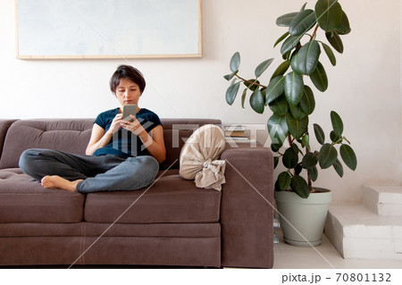 Young woman with short hair style siting on couch and talking on phone at home 70801132