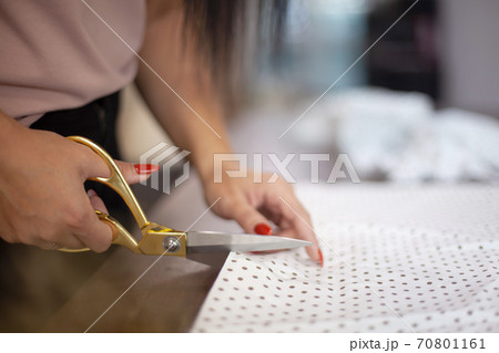 Well groomed woman hands cutting polka dot fabric with tailor scissors for sewing dress in studio Well groomed woman hands cutting polka dot fabric with tailor scissors for sewing dress in studio 70801161