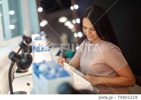 Beautiful woman tailor with long dark hair completing work with sewing machine at workplace 70801229