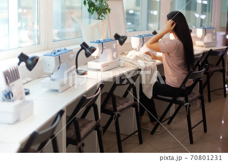 Beautiful woman tailor with long dark hair completing work with sewing machine at workplace 70801231