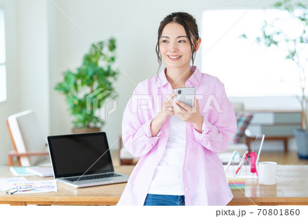 テレワーク リビングでスマホを操作する笑顔の若い女性 テレワーク リビングでスマホを操作する笑顔の若い女性 70801860