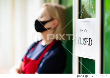 Owner hanging closed sign board on shop entrance. 70802707