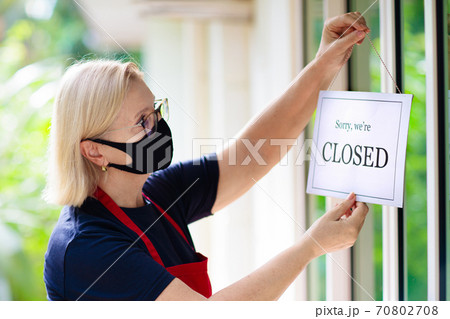 Owner hanging closed sign board on shop entrance. 70802708