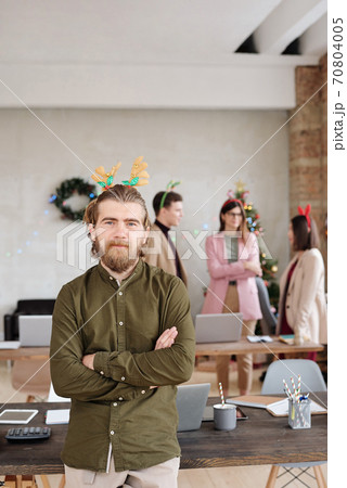 Happy young bearded businessman in xmas headwear crossing his arms on chest Happy young bearded businessman in xmas headwear crossing his arms on chest 70804005