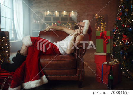 Vile Santa claus in red cap smoking cigar on couch 70804652