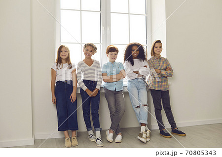 Group of happy diverse kids standing by the window, looking at camera and smiling Group of happy diverse kids standing by the window, looking at camera and smiling 70805343