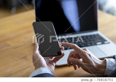 ノートパソコンの前でスマートフォンを持つ男性 70816751