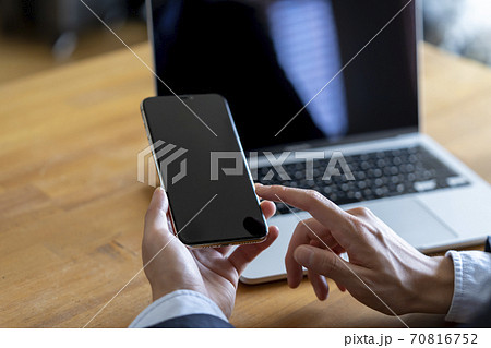 ノートパソコンの前でスマートフォンを持つ男性 70816752